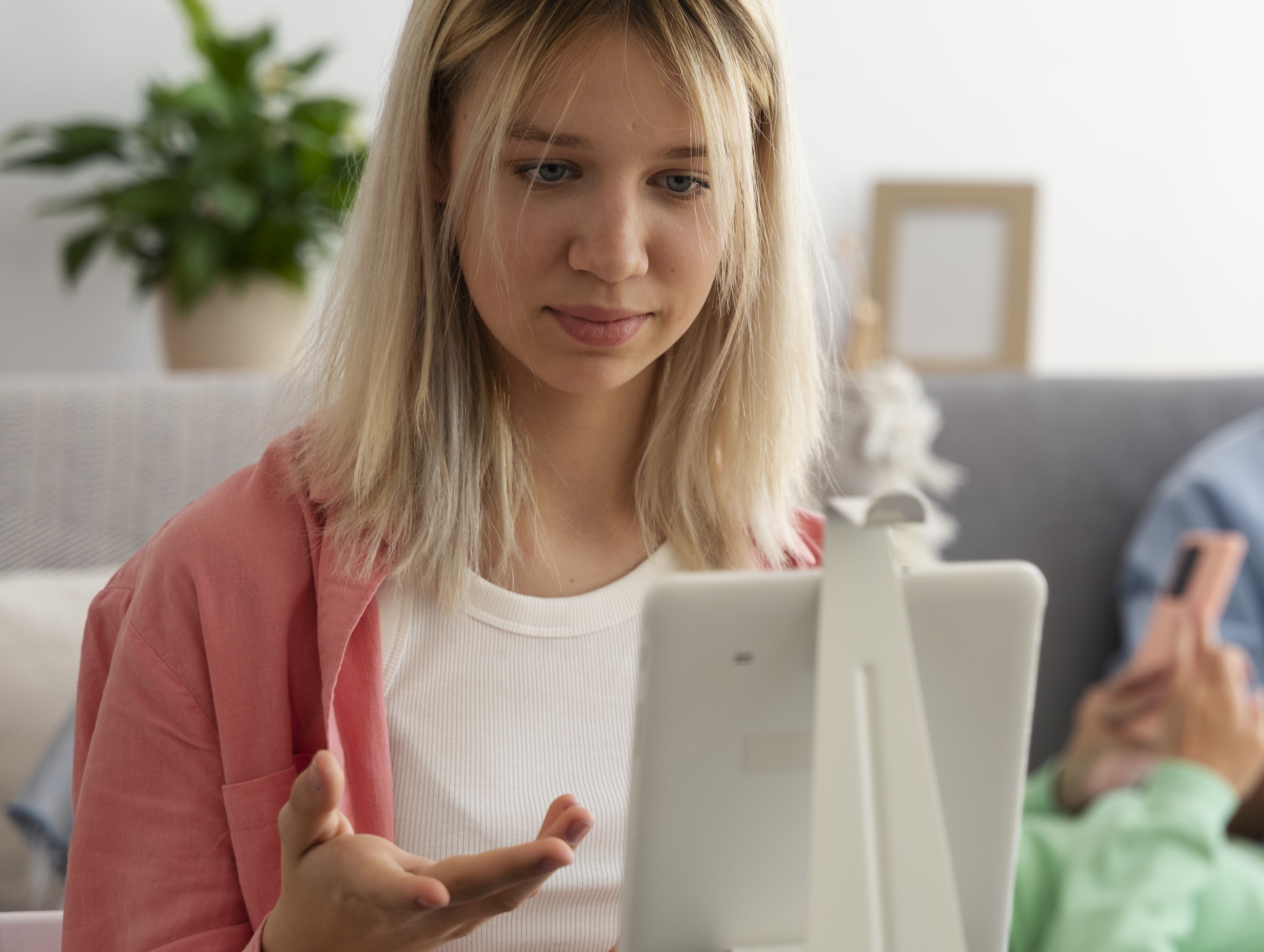 Alt-text: Uma jovem loira de camisa rosa faz acompanhamento online através de um tablet.